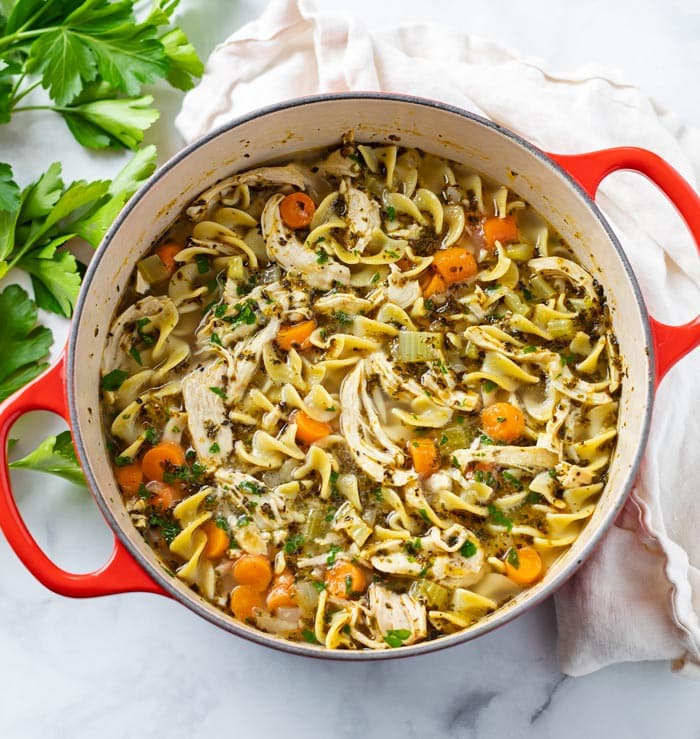 A soup pot filled with Chicken Noodle Soup with parsley on the side.