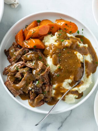 Mississippi Pot Roast on a white plate with carrots, mashed potatoes, and gravy.