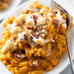 A white plate with Sweet Potato topped with Pecans and Marshmallows.