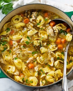 A soup pot filled with Chicken Tortellini Soup with a ladle in it.
