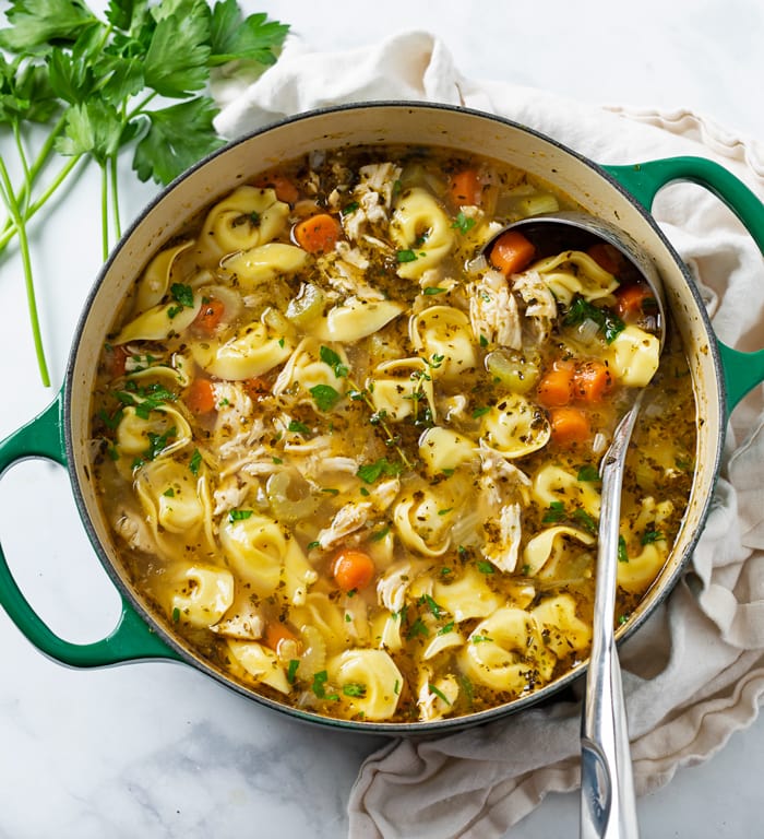 A soup pot filled with Chicken Tortellini Soup with a ladle in it.