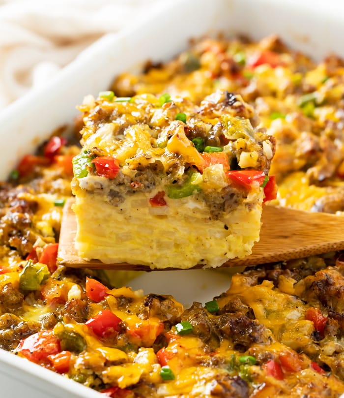 A wooden spatula holding up a slice of Hashbrown Breakfast Casserole with sausage, peppers, and cheese.