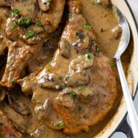 Mushroom Pork Chops in a skillet with gravy and fresh parsley.
