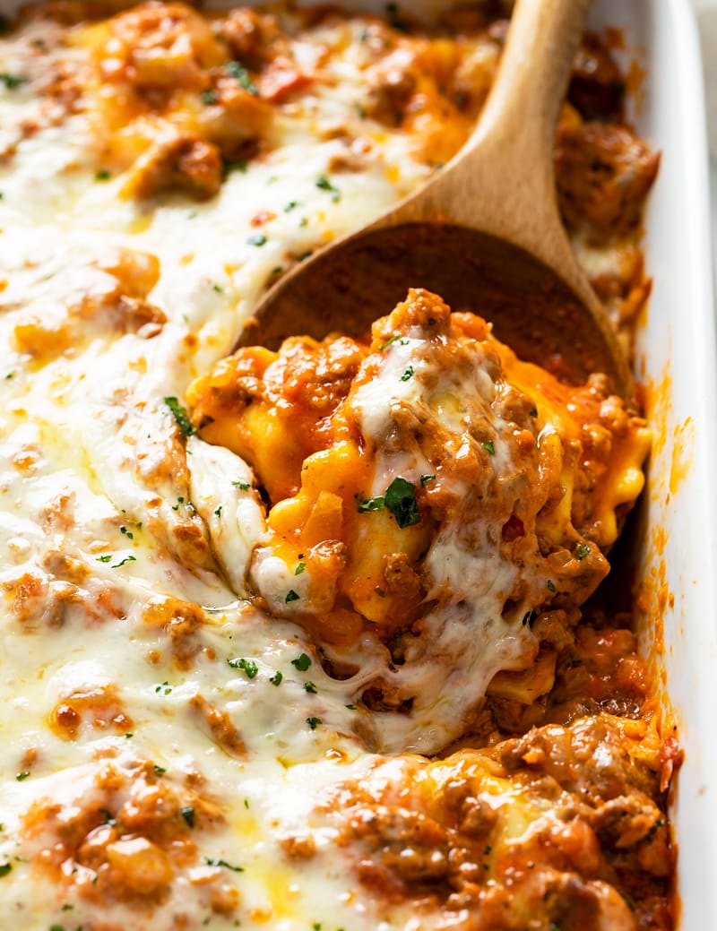 A wooden spoon scooping up baked ravioli from a casserole dish.