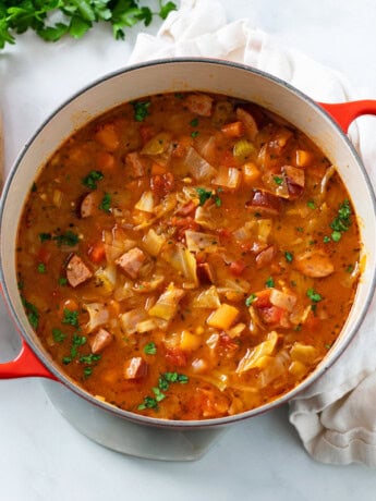 A red Dutch oven filled with Cabbage Soup with vegetables and Kielbasa.
