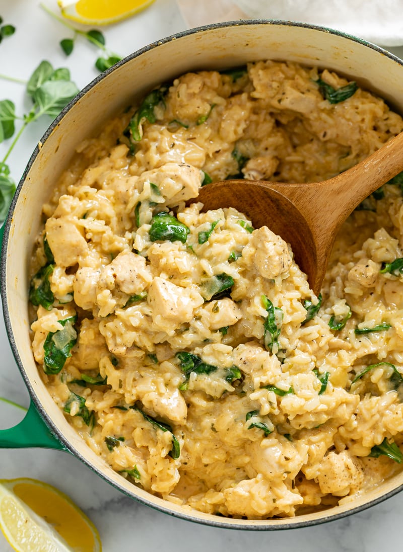 A dutch oven with Creamy Chicken and Rice with Spinach and a wooden spoon scooping it up.