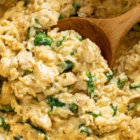A wooden spoon scooping up Creamy Chicken and Rice from a pot.