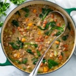 A soup pot filled with Pinto Bean Soup with a ladle and parsley on the side.