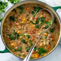 A soup pot filled with Pinto Bean Soup with a ladle and parsley on the side.