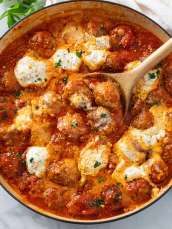 Ricotta Meatballs in tomato sauce with herb ricotta cheese and a wooden spoon.