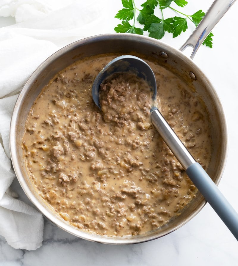 A skillet filled with Hamburger Gravy with a ladle in it.