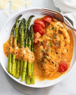 Creamy Tomato Chicken on a white plate next to asparagus with cherry tomatoes.
