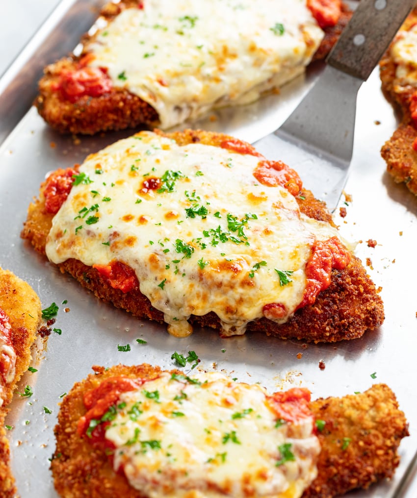 Chicken Parmesan on a tray with marinara sauce, mozzarella, and fresh parsley. 
