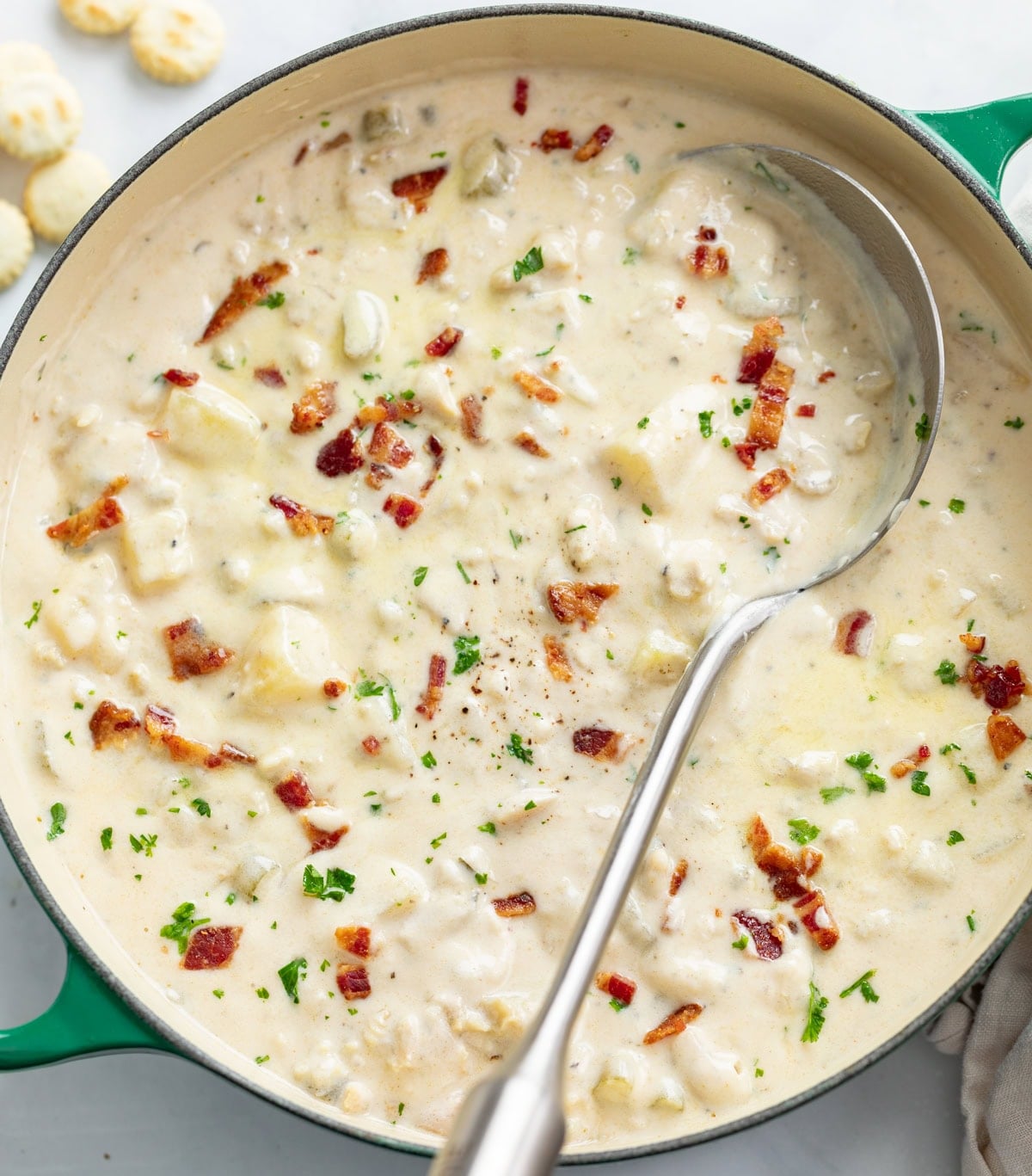 Clam Chowder in a soup pot with a spoon on the side and chopped bacon on top.