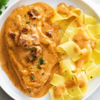 A white plate with Marry Me Chicken with a side of pappardelle pasta.