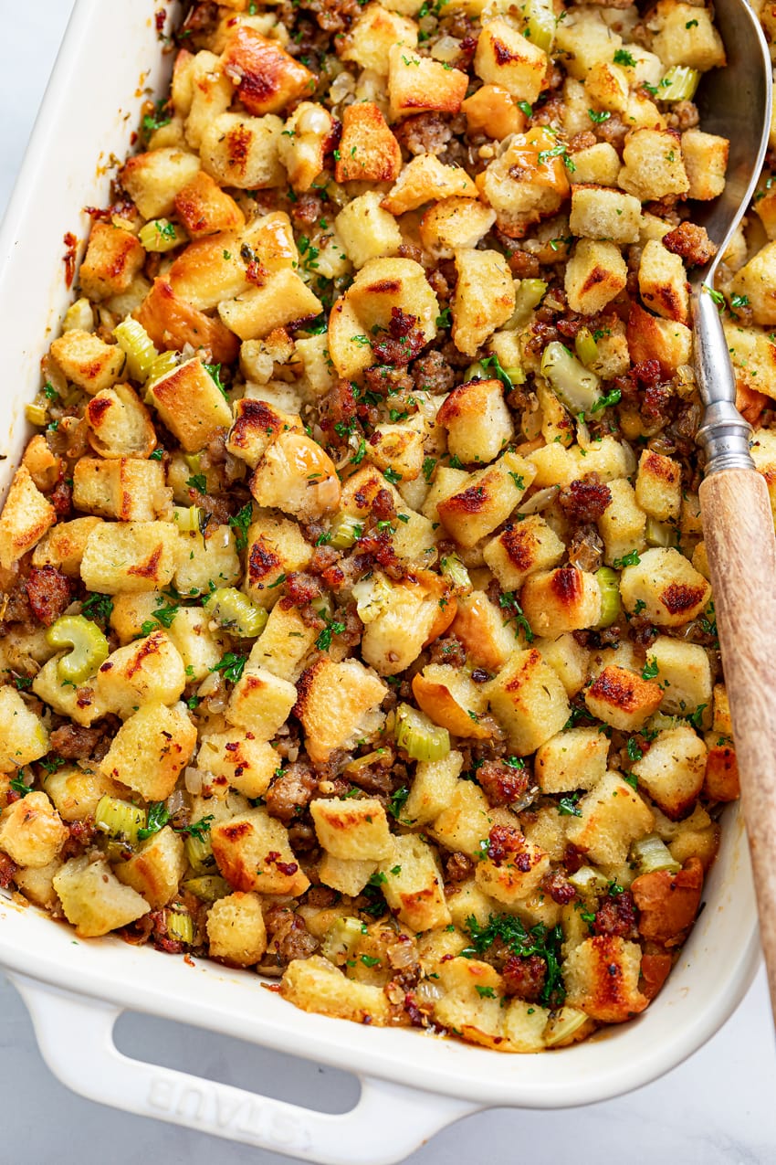 A white casserole dish with Sausage Stuffing and a spoon on the side.