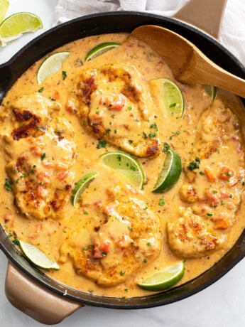 Cajun Chicken in a skillet with sauce and lime wedges with fresh cilantro.