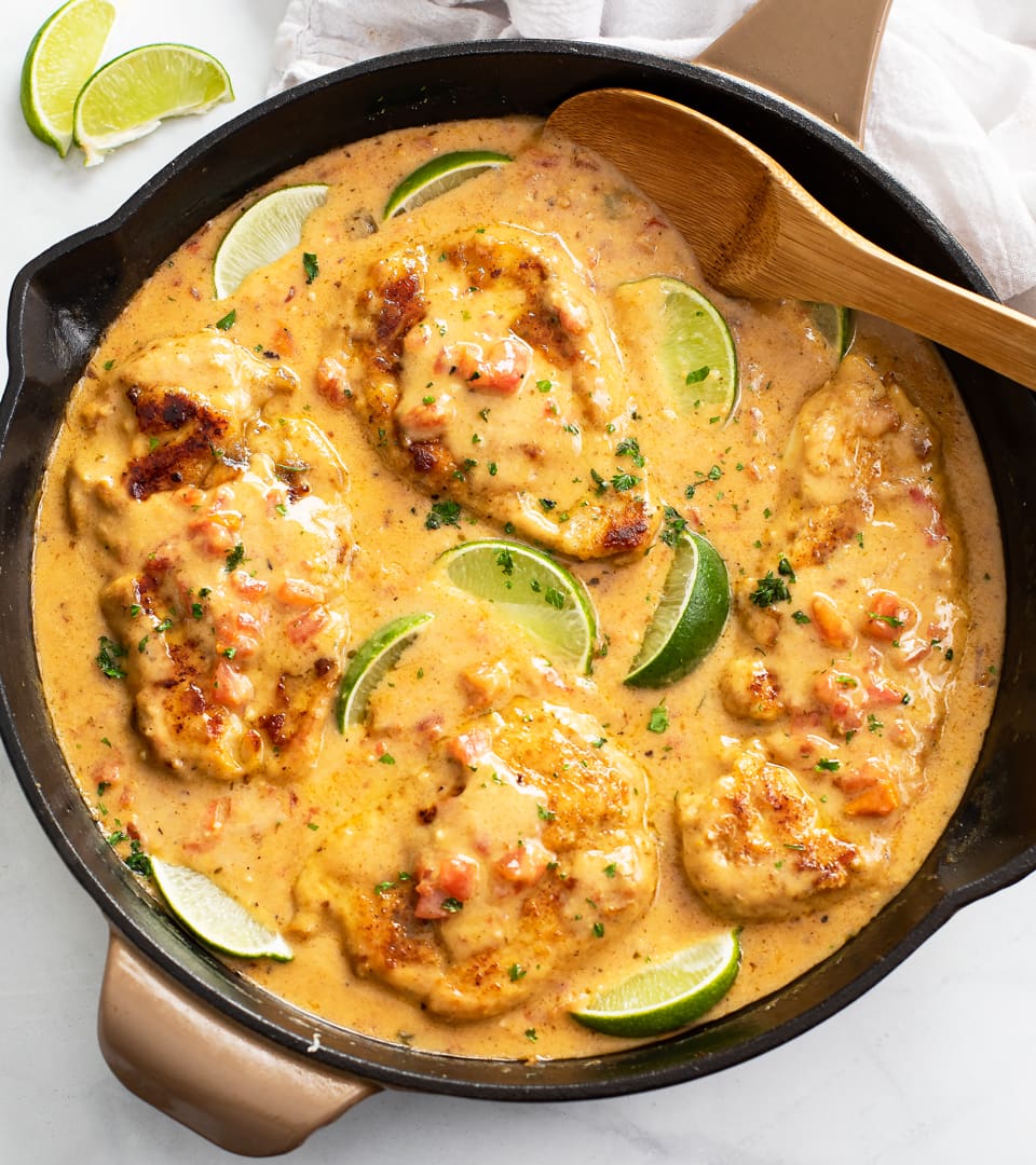 Cajun Chicken in a skillet with sauce and lime wedges with fresh cilantro.