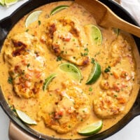 Cajun Chicken in a skillet with a wooden spoon and lime wedges.