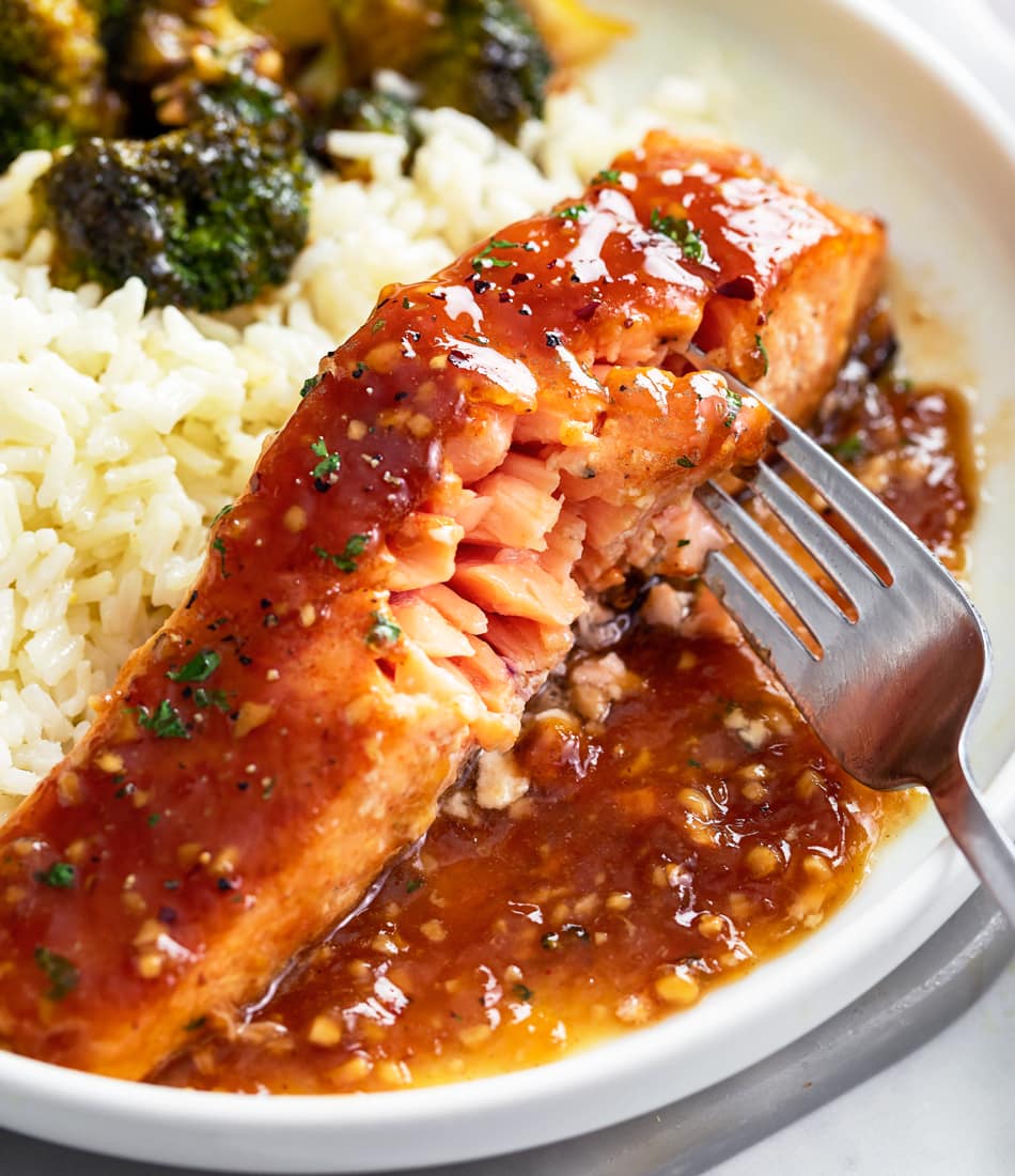A fork touching the surface of cooked salmon to reveal flaky layers.