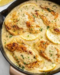 Lemon Pepper Chicken in a skillet with lemon wedges and sauce.