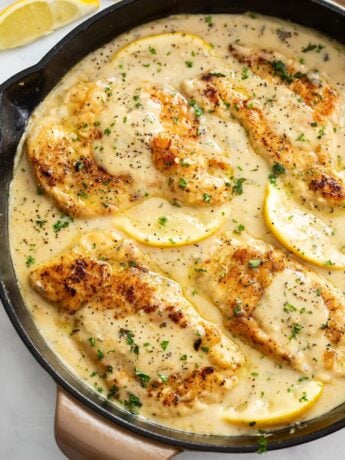 Lemon Pepper Chicken in a skillet with lemon wedges and sauce.