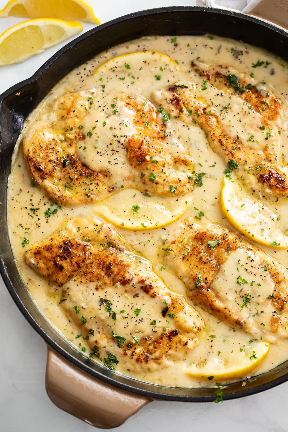 Lemon Pepper Chicken in a skillet with lemon wedges and sauce.