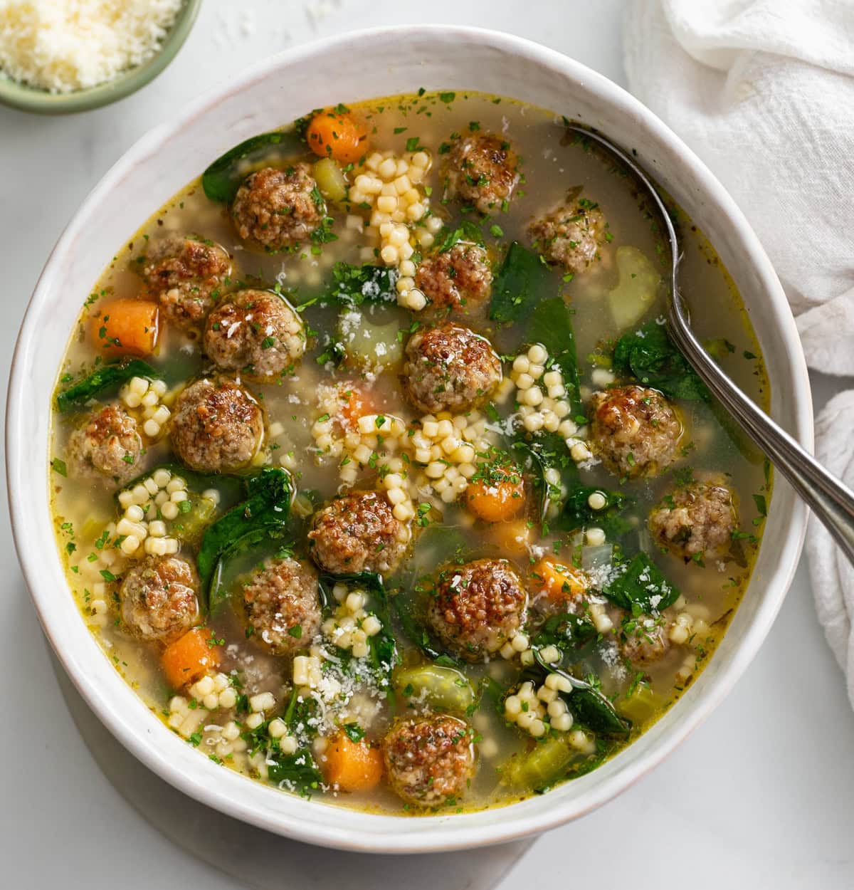 Italian Wedding Soup in a white bowl with a spoon on the side.