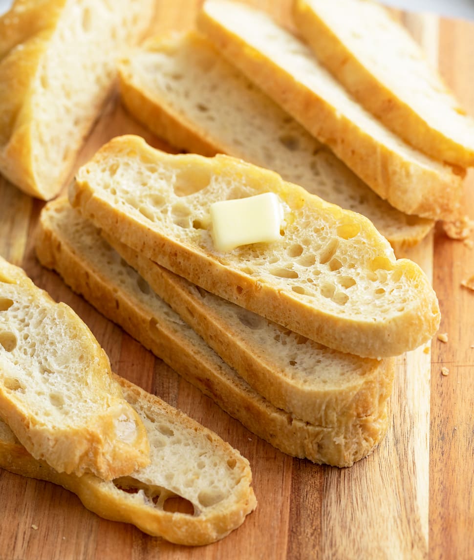 Slices of No Knead Bread stacked on a cutting board with butter on top.