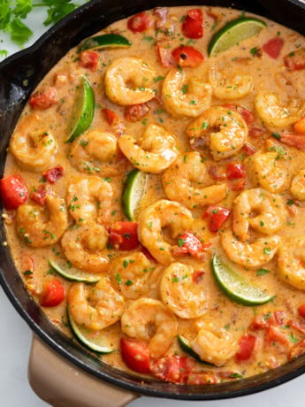 Cajun Shrimp in a skillet with sauce, bell peppers, and lime wedges.