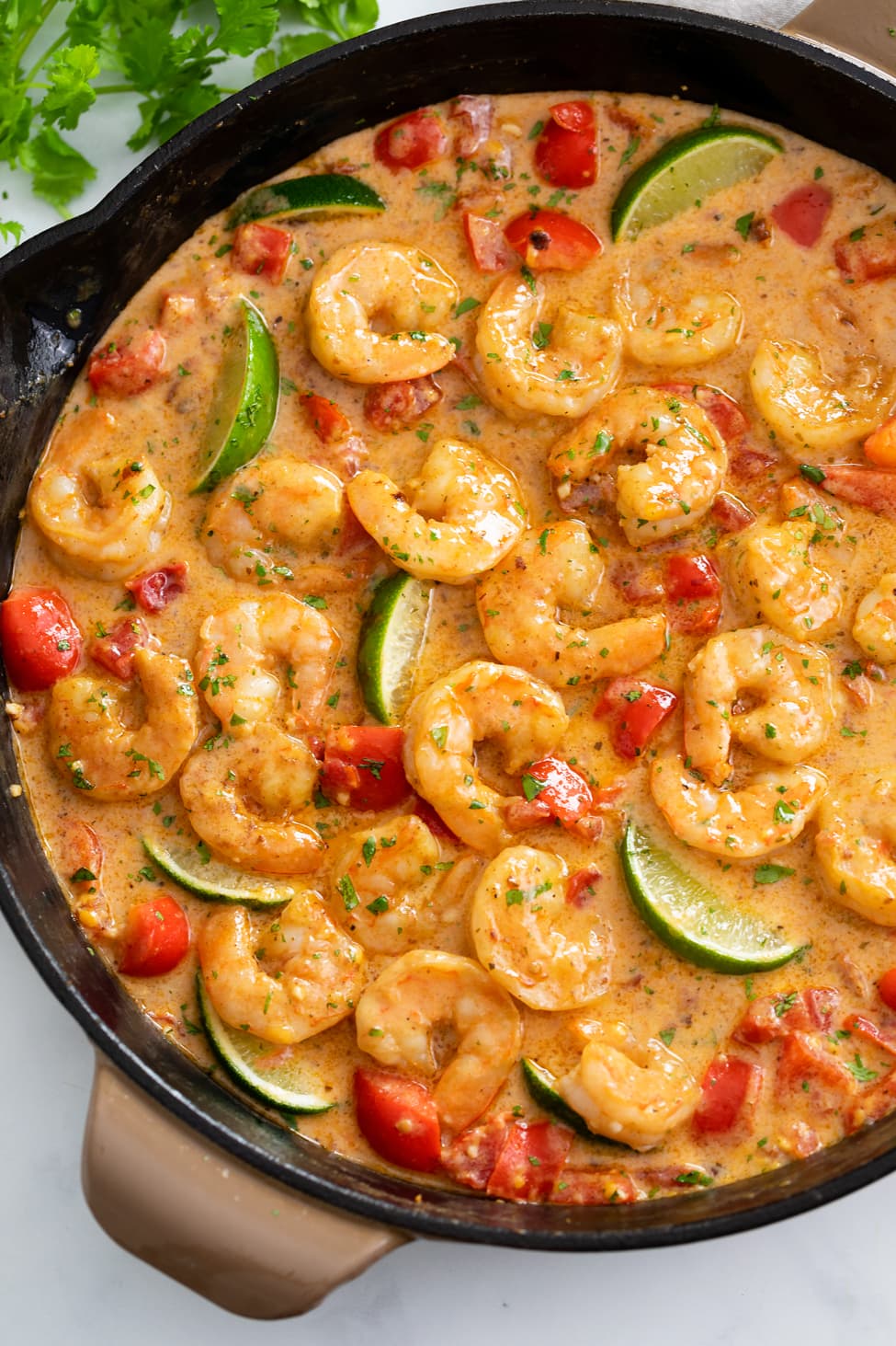 Cajun Shrimp in a skillet with sauce, bell peppers, and lime wedges.