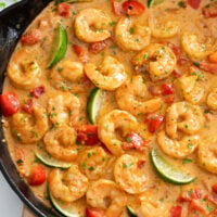 Cajun Shrimp in a skillet with Cajun sauce. bell peppers, and lime wedges.