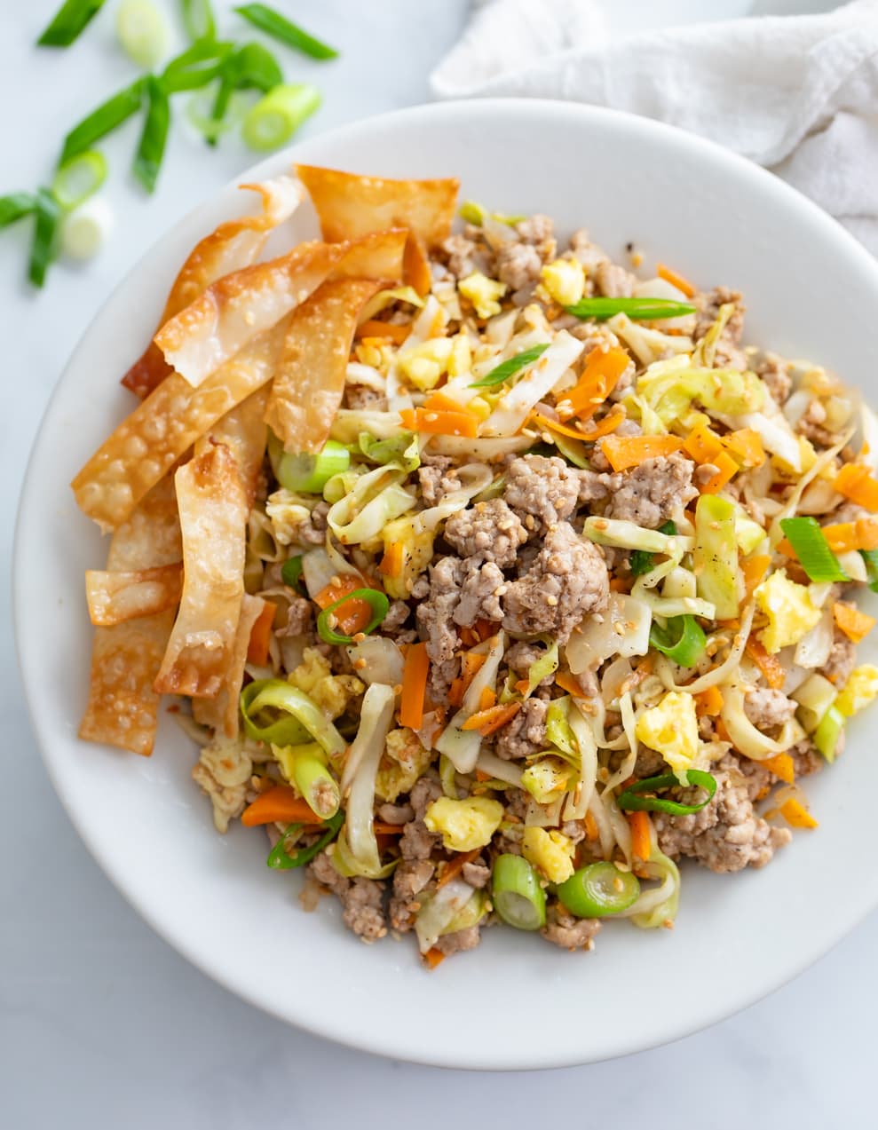 A white bowl filled with Egg Roll in a Bowl with crispy fried egg roll wraps on the side.