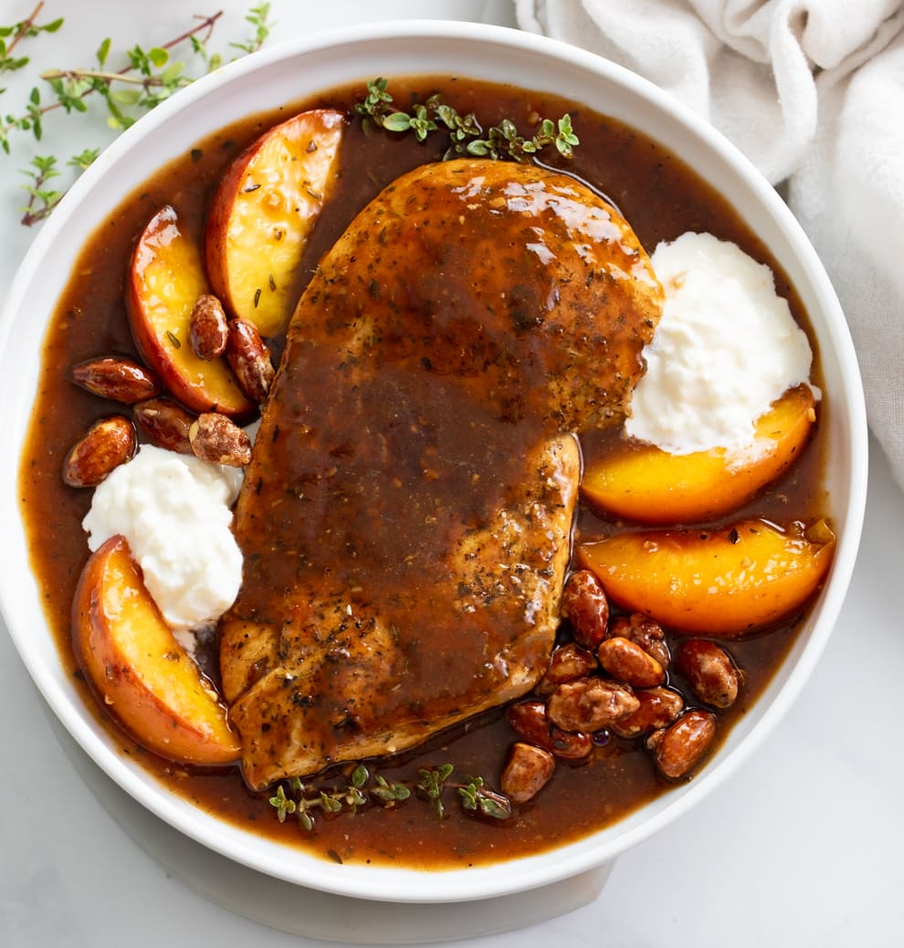 Peach Chicken on a White Plate with peaches, burrata and a balsamic sauce.