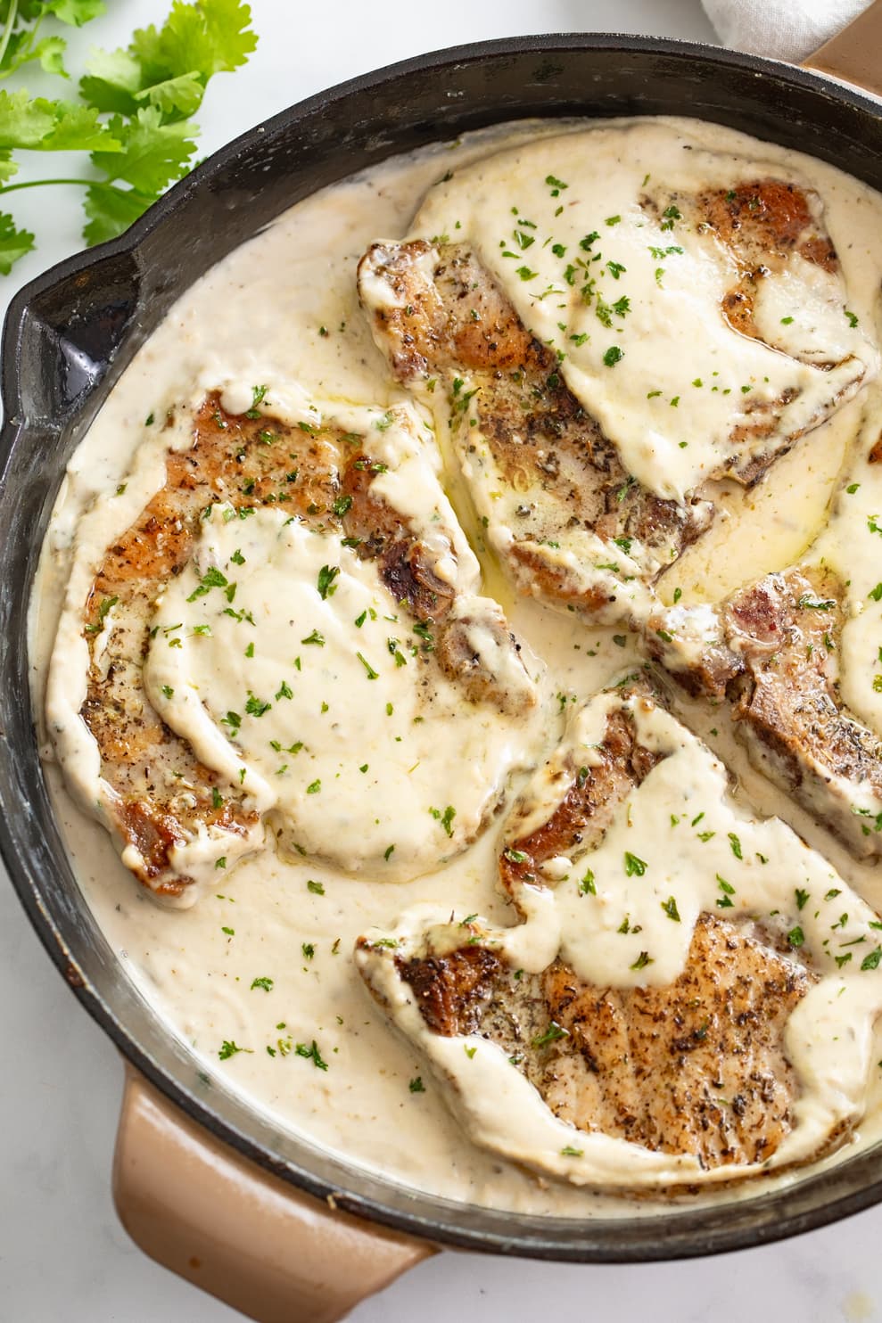 Ranch Pork Chops in a skillet with ranch sauce topped with parsley.