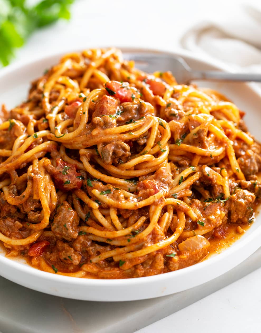 A white plate with Taco Spaghetti with taco meat and diced tomatoes.