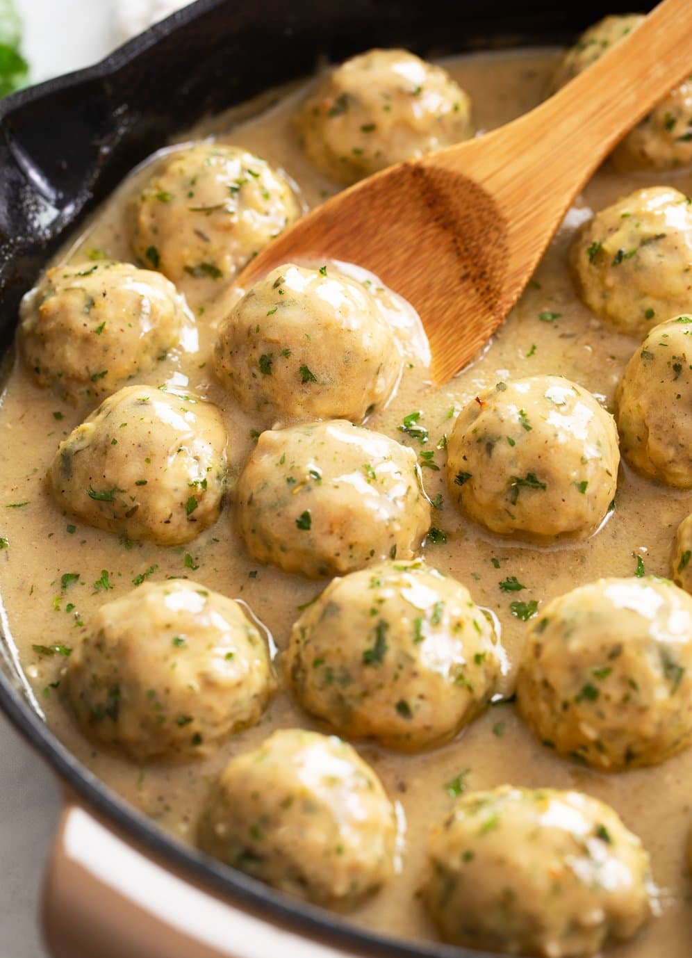Chicken Meatballs in a skillet with sauce and a wooden spoon.