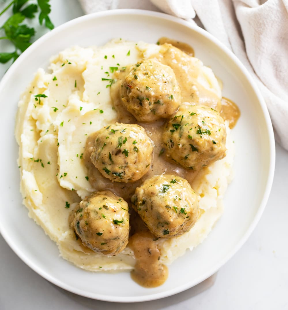 Chicken Meatballs and sauce on top of mashed potatoes on a white plate.