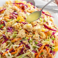 A spoon drizzling dressing on top of Ramen Noodle Salad.