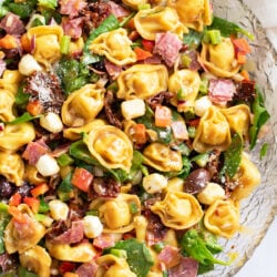 Tortellini Pasta Salad in a glass bowl with vegetables, mozzarella pearls, and more.
