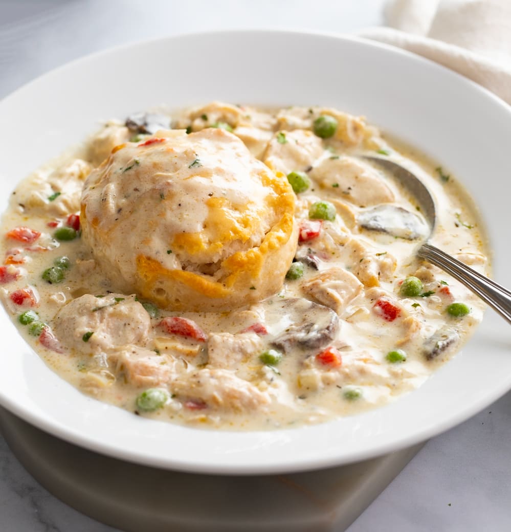 Chicken a la King in a white bowl with a biscuit on top.