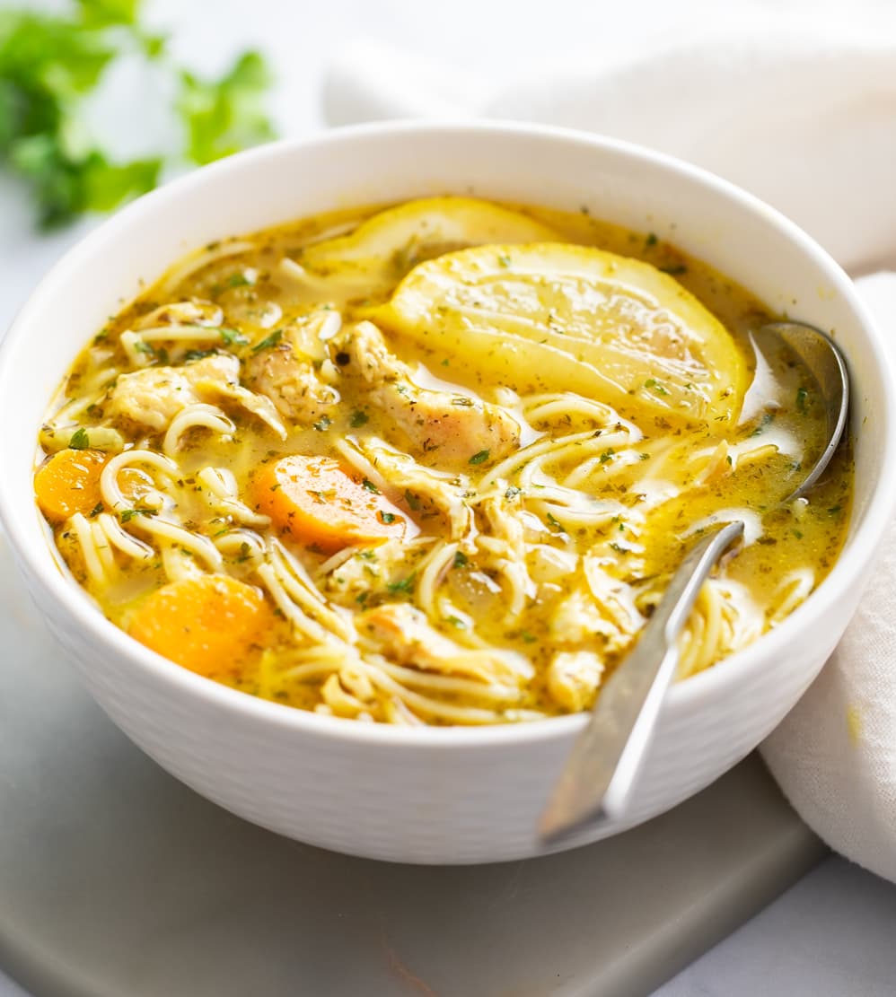 A white bowl of Lemon Chicken Soup with a spoon on the side.