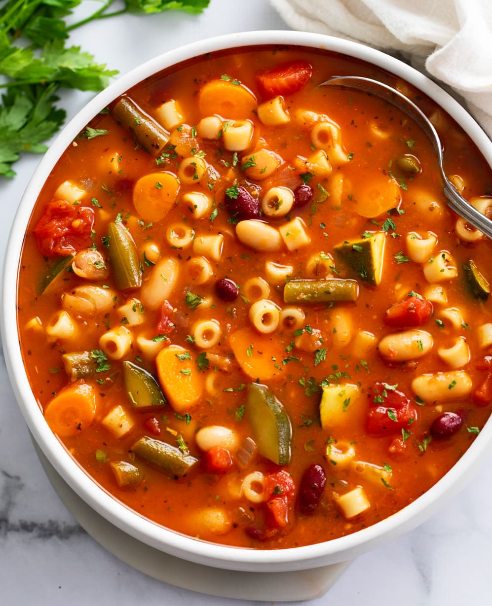 Minestrone Soup in a white bowl with a spoon on the side.