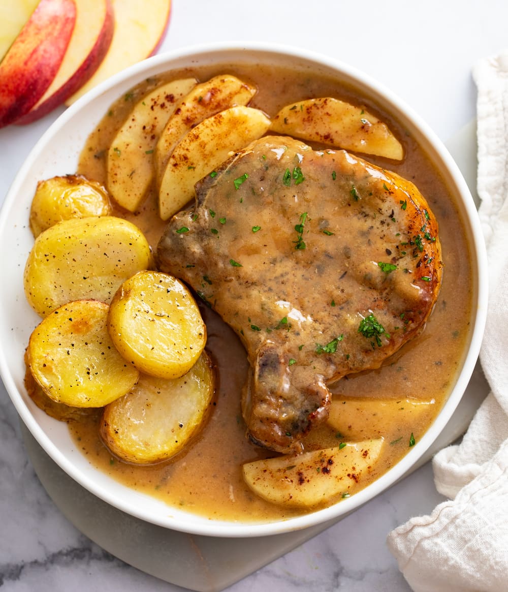 Apple Pork Chops on a white plate next to roasted potatoes.