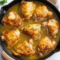 A skillet filled with Baked Chicken Thighs in sauce with fresh thyme on top.