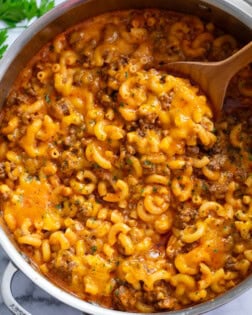 Beefaroni in a skillet with a wooden spoon scooping it up.