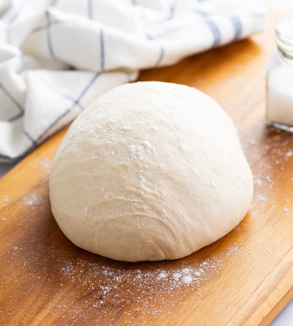 A ball of pizza dough topped with flour on a wooden surface.