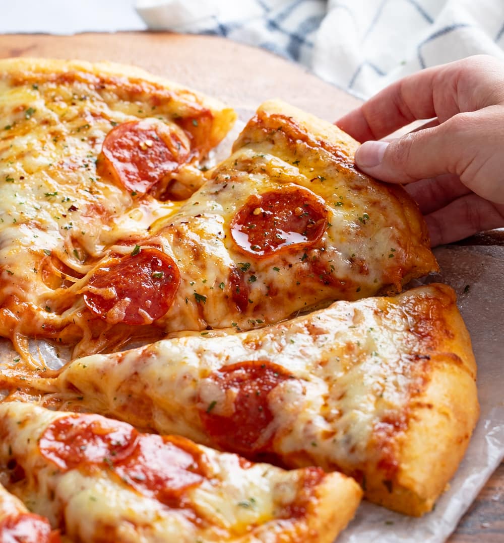 A hand pulling up a slice of cheesy pepperoni pizza.