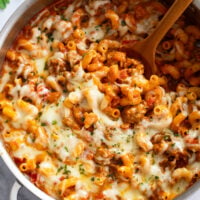 A skillet filled with Italian Sausage Pasta with a wooden spoon.