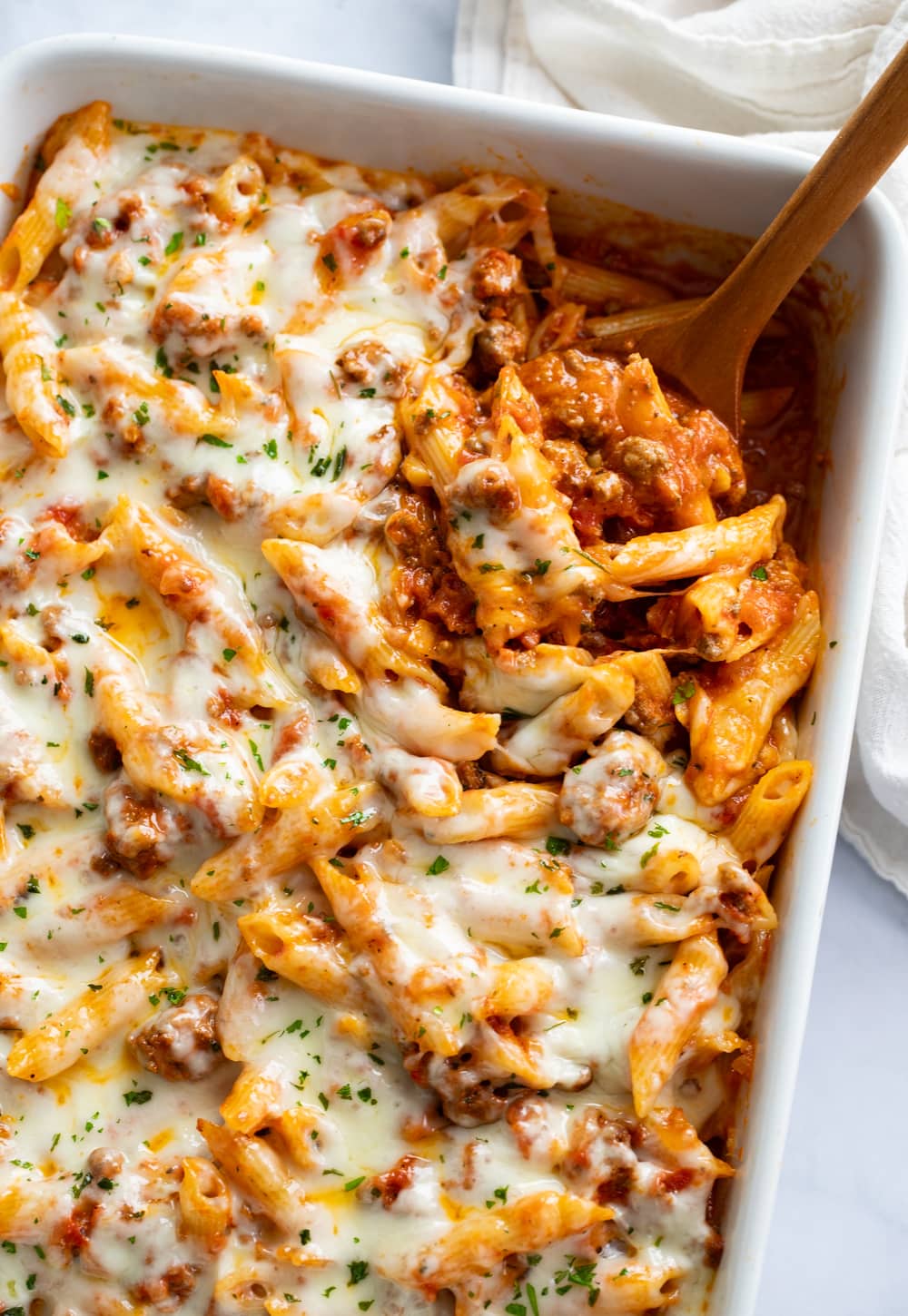 Ground Beef Casserole in a white baking dish with a wooden spoon scooping it out.